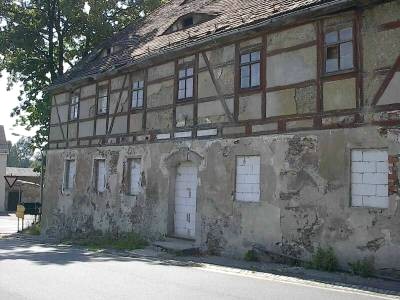 Verfallenes Fachwerkhaus mit abblätterndem Putz; die Fenster und die Tür im Erdgeschoss sind zugemauert.