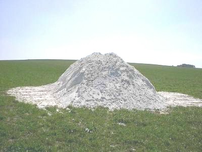 Kegelförmiger Haufen aus weißem, pulvrigem Material liegt auf einer grünen Wiese unter hellem Himmel.