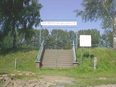 Breite Steintreppe mit Geländern führt eine Böschung hinauf; darüber ein Schild „TSV 1875 Großwaltersdorf e. V.“, daneben eine leere weiße Tafel.